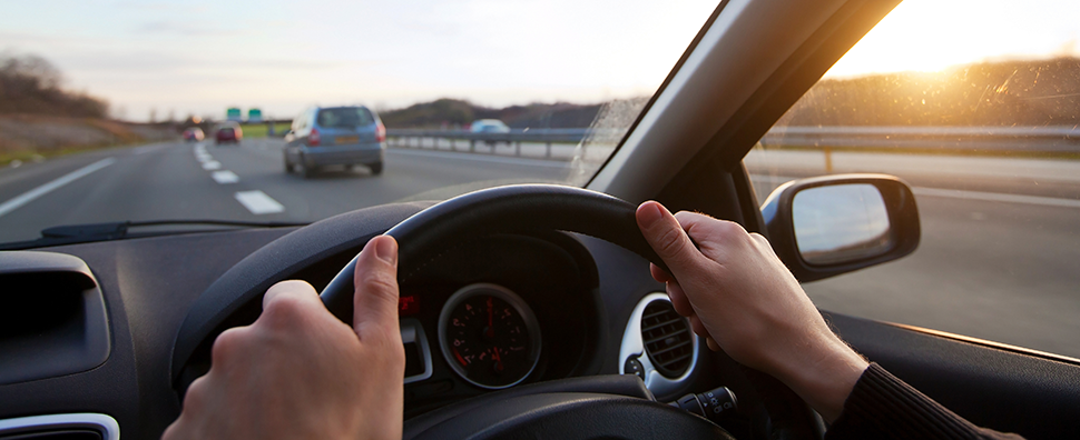 Person's hands on steering wheel driving on a motorway