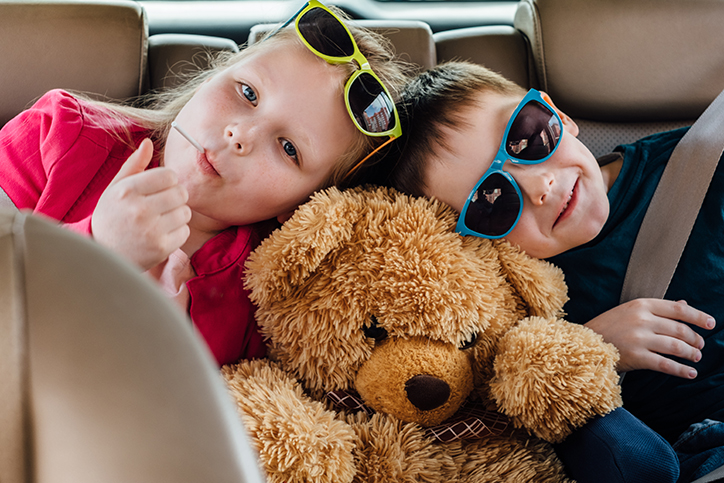 Two kids in the backseat of a car with a teddy