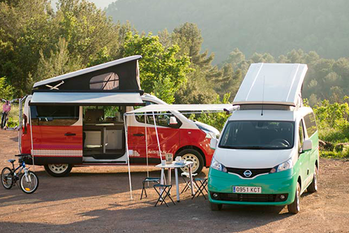 Two Nissan electric camper vans set up in the countryside for a camping trip