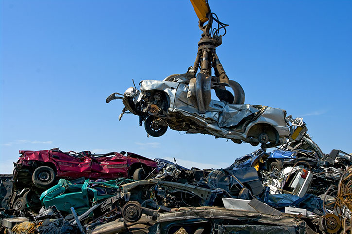 Scrap car being lifted by a claw from a pile of other scrap cars